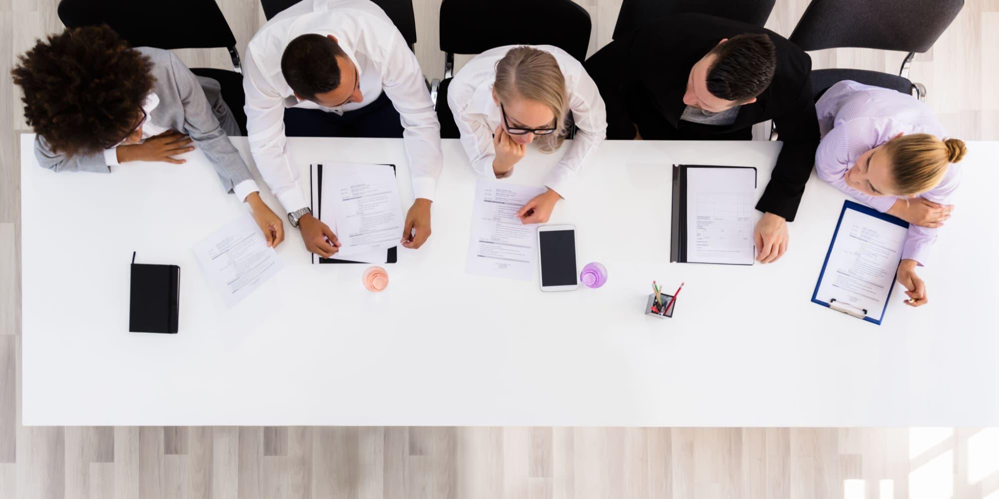 Five people sit at a white rectangular table viewed from above 