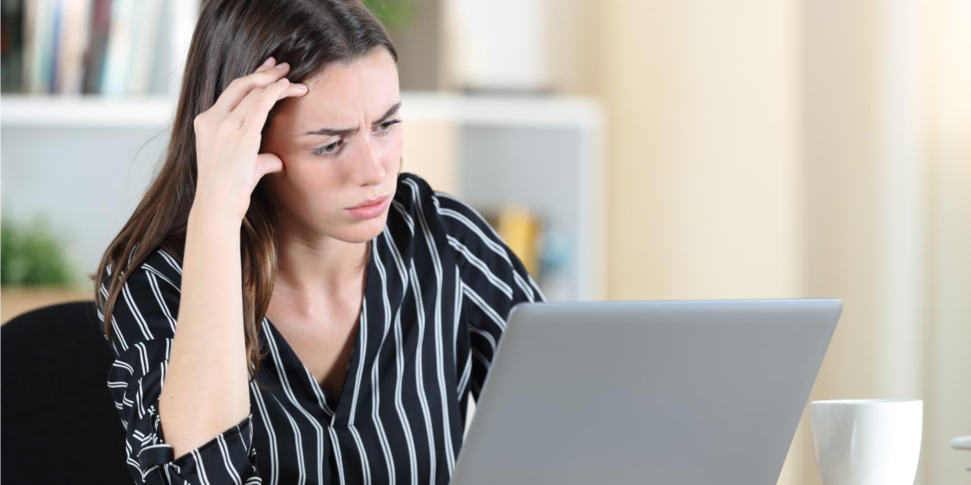 Young woman stares on computer screen with frustration and hand on forehead